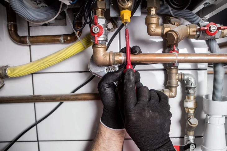 Intérieur d'installation technique avec technicien portant gants de protection orange travaillant sur système de plomberie