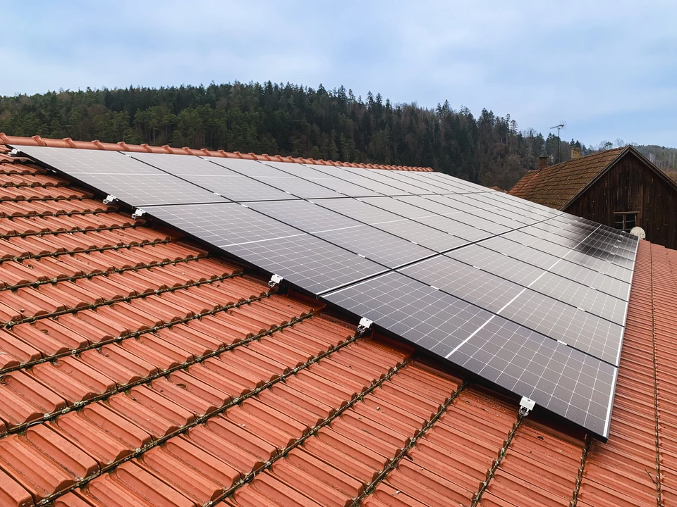 Maison résidentielle avec panneaux solaires photovoltaïques installés sur toiture en tuiles, éclairée par soleil couchant