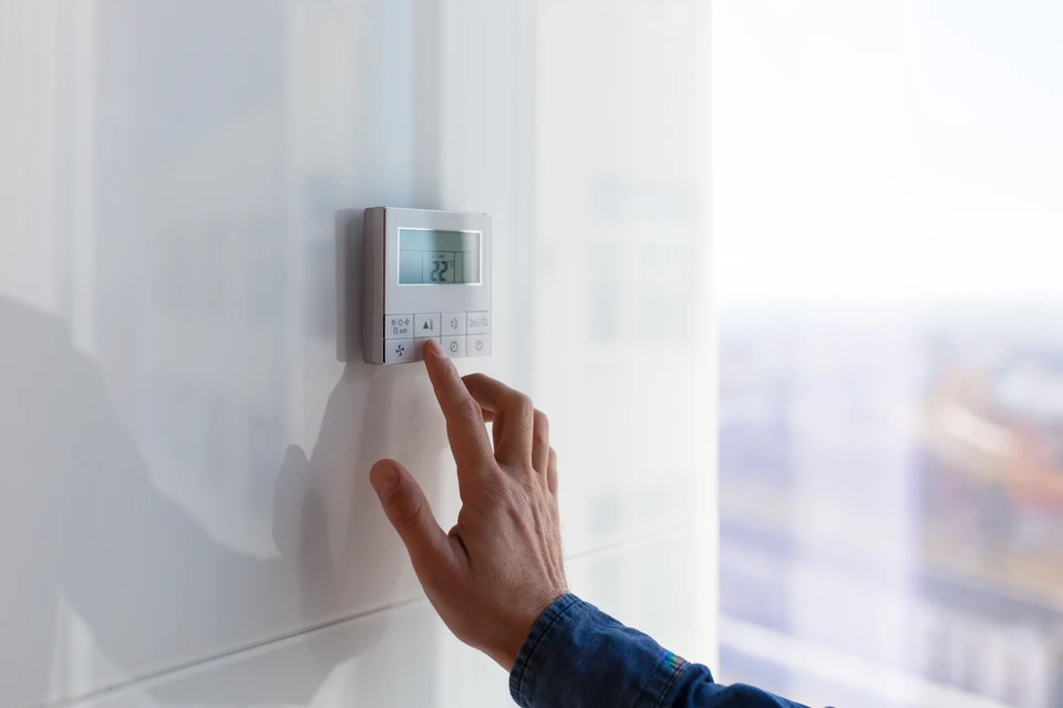 Une main masculine ajuste un thermostat mural digital blanc dans un intérieur résidentiel moderne