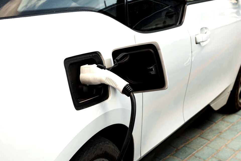 Scène extérieure urbaine avec véhicule électrique en charge sur voie pavée, environnement verdoyant avec arbres en arrière-plan, ambiance résidentielle calme