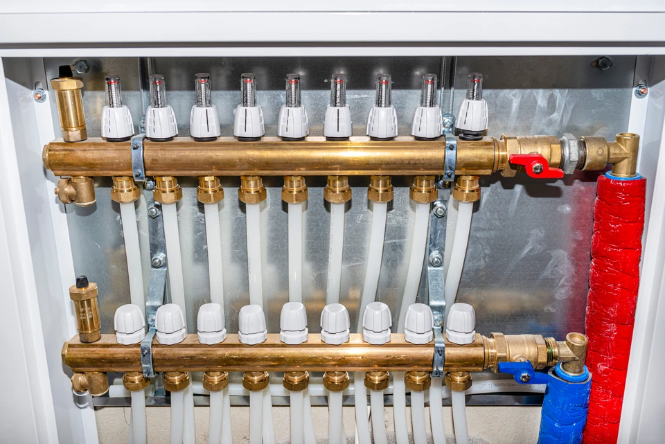 Installation de chauffage moderne avec chaudière murale blanche, système de distribution hydraulique en cuivre, collecteurs de distribution, vannes de régulation et manomètres
