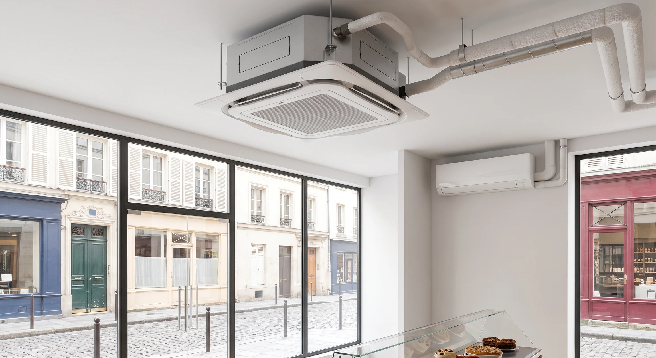 Gros plan professionnel d'une unité de climatisation commercial montée en plafond ou en mural dans un espace commercial (magasin, boucherie, fromagerie ou boulangerie), montrant clairement les grilles de diffusion, les tuyauteries et le système moderne. L'image doit mettre en avant le matériel technique de refroidissement dans un contexte commercial réel et professionnel, sans focus sur les produits ou les personnes.